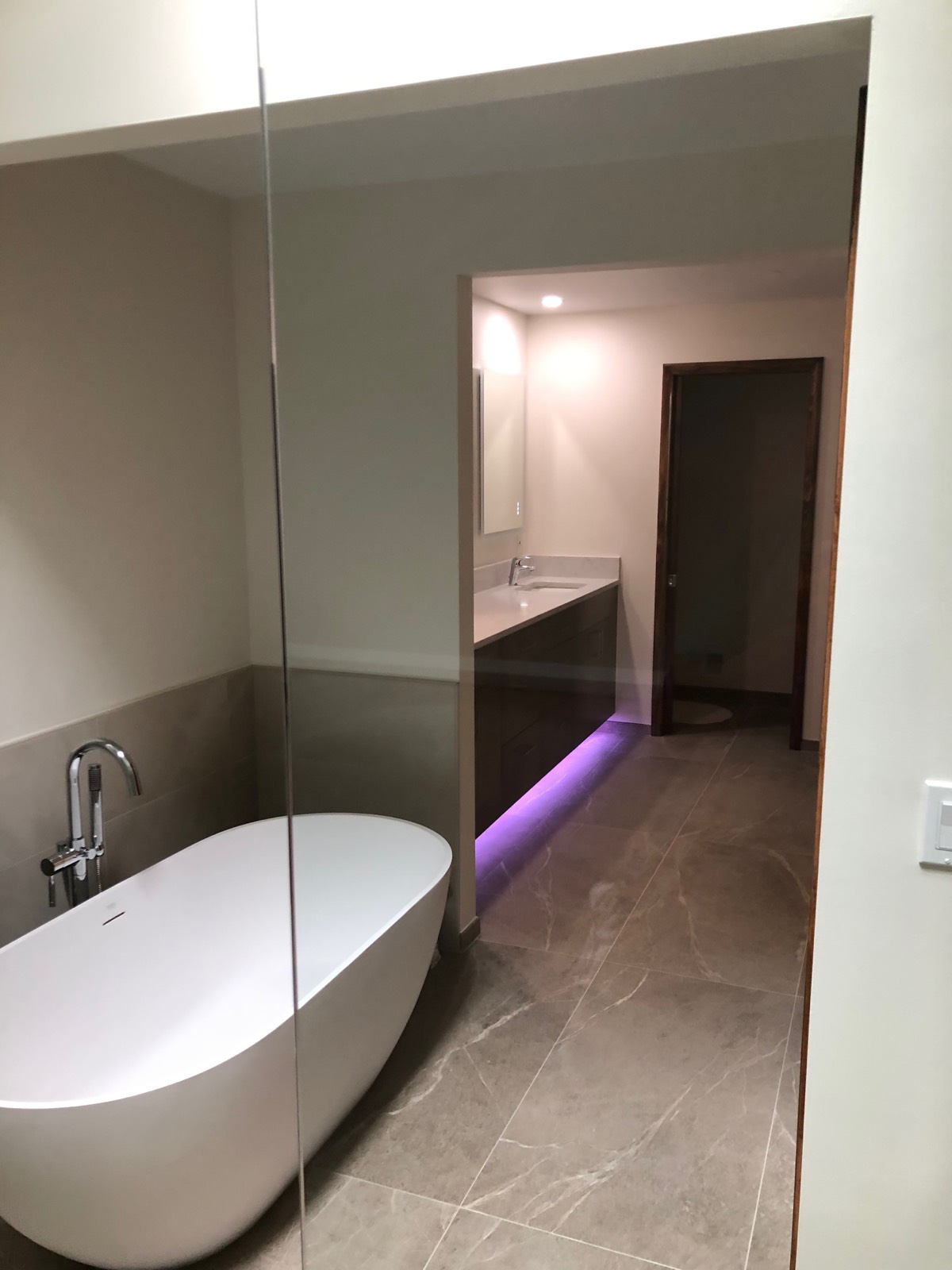 View past a freestanding tub to a floating walnut vanity with LED toe-kick lighting