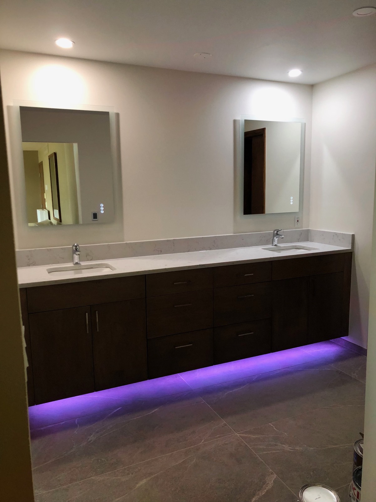 Floating double vanity in dark wood with backlit mirrors and an LED glow beneath