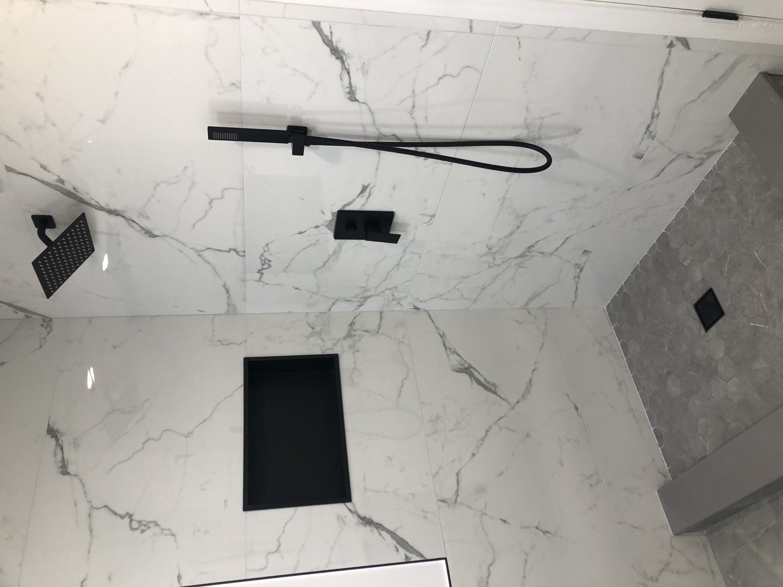 Marble-look porcelain shower with a recessed black niche, matte black rain head and handheld, and a curb