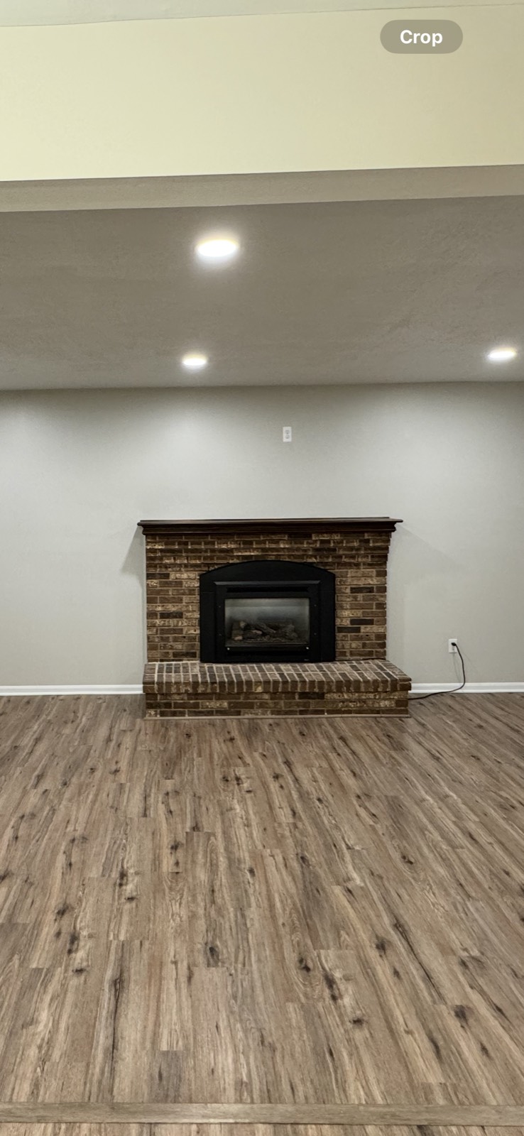 Basement with an unpainted red brick fireplace and wood mantel
