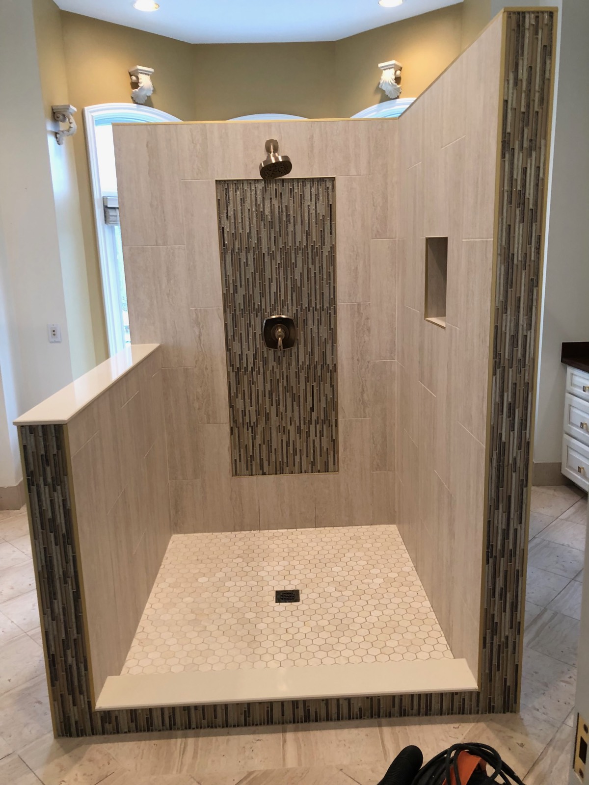 Walk-in shower with a half wall, glass mosaic accent panel and trim, and a hexagon mosaic floor